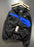 A black Nike windbreaker jacket with bright blue color-blocked panels on the chest, hanging on a wooden hanger against a dark gray wall. The jacket features a white Nike swoosh on the left chest and a hangtag is attached.