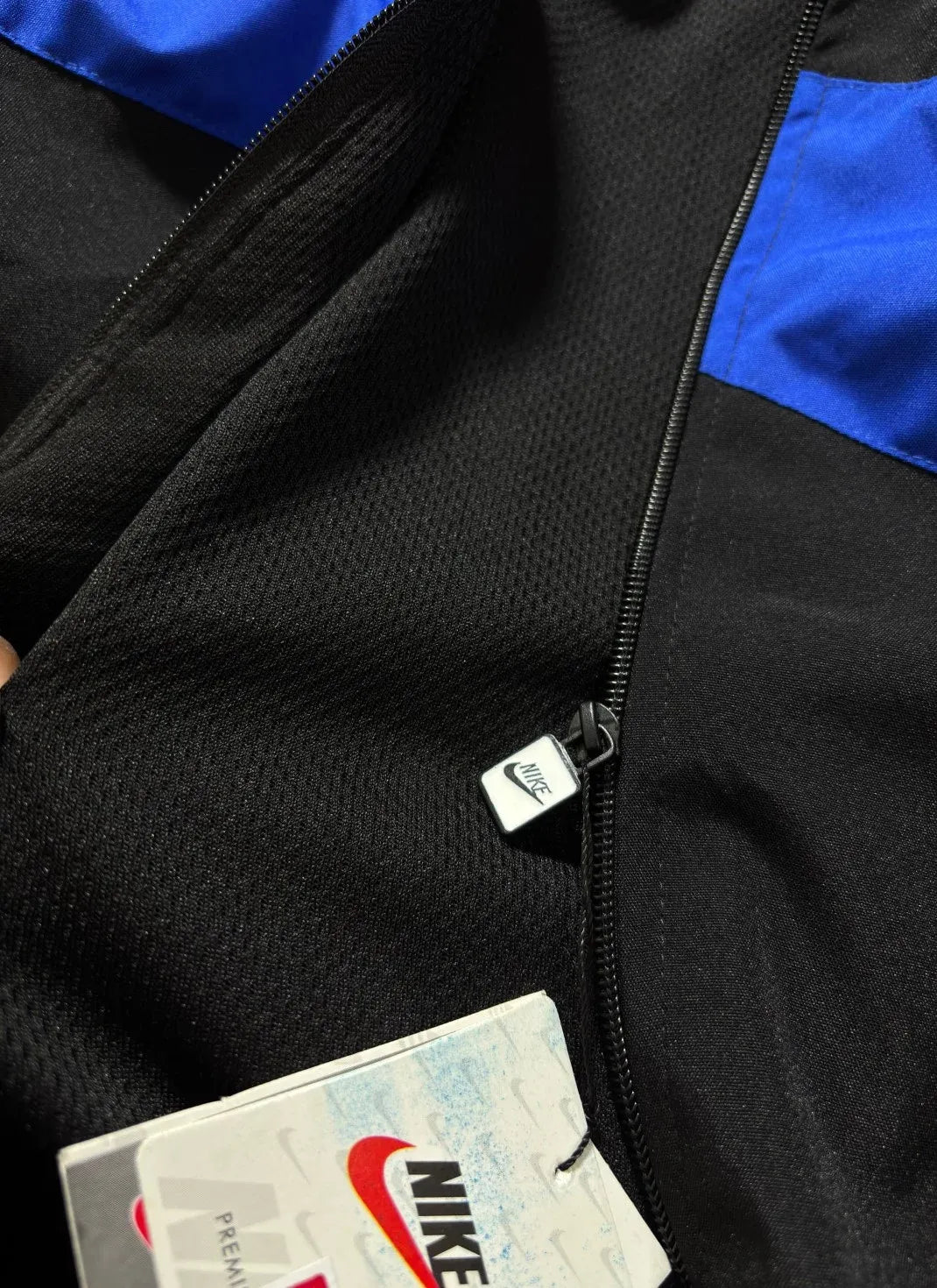 Close-up of a black Nike zip-up jacket with bright blue shoulder panels and a visible Nike hangtag.