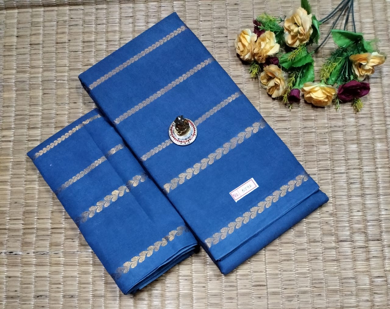 Blue saree with silver stripes on a woven surface with decorative flowers.