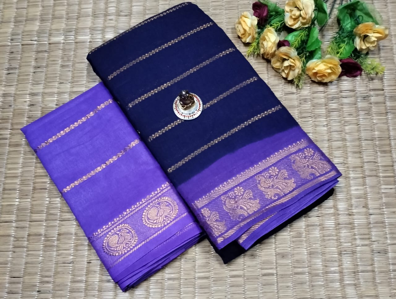 Two blue sarees with gold patterns on a woven surface.