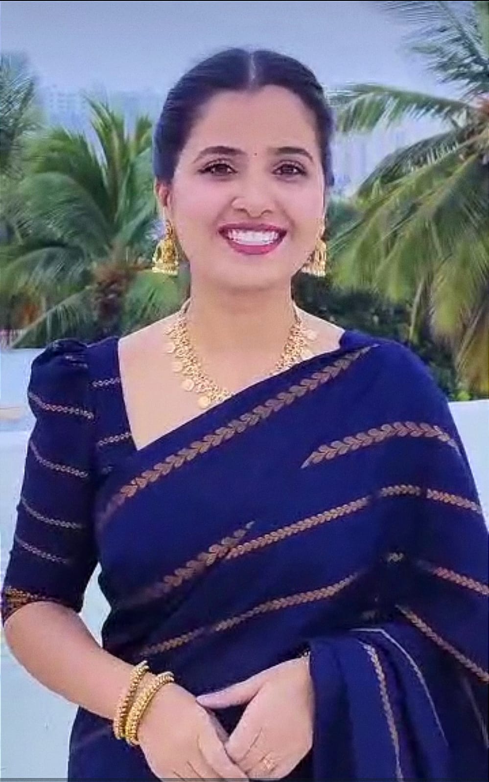 Woman in a blue saree with gold patterns against a tropical background