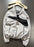 A light gray Nike windbreaker jacket with a black diagonal chest stripe and black zippers, hanging on a wooden hanger against a dark gray wall.