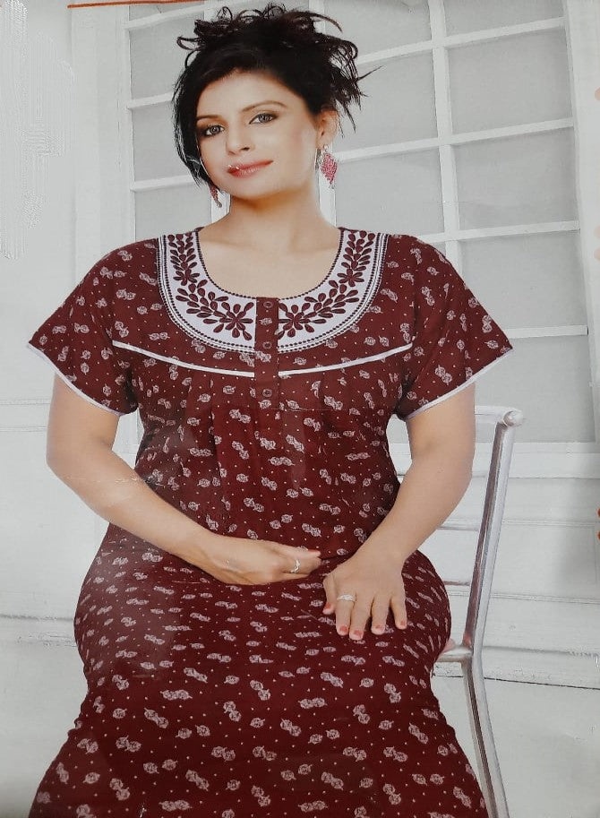 Woman wearing a maroon dress with white patterns in a room with white walls and a chair.