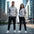 Two people wearing matching gray hoodies and black pants in an urban setting.